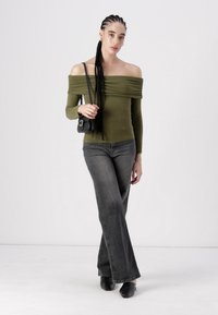 Oliven off-shoulder topp med drapert stoff, kombinert med høyt liv mørkegrå buksene med utvidet ben og svarte slip-on sko, holdt svart håndveske.