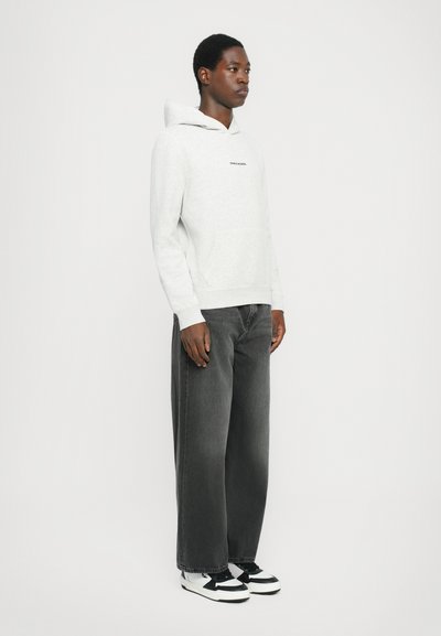Haut à capuche gris clair avec une poche avant, texte en logo noir, associé à un jean large gris foncé et des baskets noir et blanc.