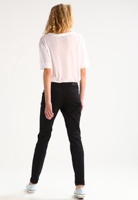 White loose-fitting T-shirt with short sleeves paired with black slim trousers. Footwear includes light blue canvas shoes.