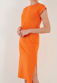 Oranžové šaty do délky kolen z měkké tkaniny, s krátkými rukávy a bočním rozparkem pro snadný pohyb. Jednoduchá, přiléhavá silueta.