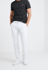 Svart kortärmad T-shirt med en liten logotyp, tillsammans med vita byxor med uppvikta ärmar och vita sneakers. Enkelt, avslappnat outfit.