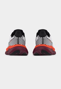 Ζευγάρι λευκών και μαύρων αθλητικών παπουτσιών με πορτοκαλί ενδιάμεσα πέλματα και μωβ εξωτερικές σόλες, εμφανιζόμενα από πίσω σε λευκό φόντο.