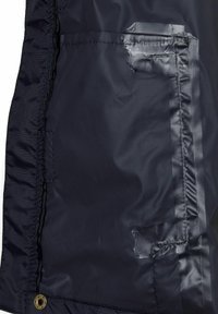 Laivastonsinisen takin vuori on sileä ja kiiltävä. Siinä on ommellut saumat ja pieni tasku läpällä. Mukana on messinginvärinen napitus.