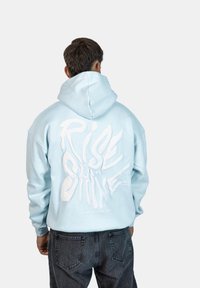 Felpa leggera di colore azzurro con vestibilità oversize, caratterizzata dalla scritta bianca "RISE & SHINE" sul retro. Tessuto testurizzato e cappuccio regolabile.