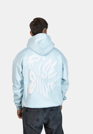 Felpa leggera di colore azzurro con vestibilità oversize, caratterizzata dalla scritta bianca "RISE & SHINE" sul retro. Tessuto testurizzato e cappuccio regolabile.