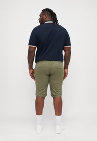 Navy polo shirt with orange and white accents, paired with olive green knee-length shorts. The outfit is completed with white sneakers and socks.