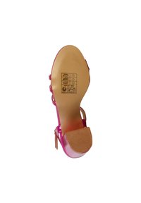 Pink patent high heel shoe with a textured sole, transparent straps, and a nude-colored footbed. Labels and care instructions visible on sole.