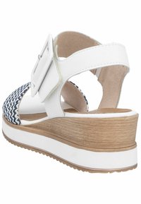 Sandale blanche avec un supérieur tissé bleu marine et blanc, talon épais, détail de boucle et accent en bois texturé sur la semelle.