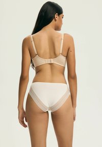 Beżowy biustonosz z regulowanymi ramiączkami i zapięciem na haftki, w połączeniu z białymi majtkami ozdobionymi koronką. Gładka tkanina i prosty design.
