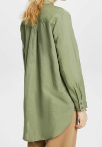 Camicia verde oliva a maniche lunghe con vestibilità rilassata, polsini abbottonati, dettaglio piega sul retro e orlo curvo, realizzata in un tessuto testurizzato.