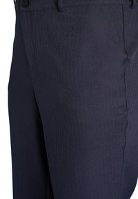 Detailný záber tmavomodrých formálnych nohavíc, ktorý zobrazuje pás, gombík, vrecko a jemnú textúru tkaniny s rybovou kostrou.