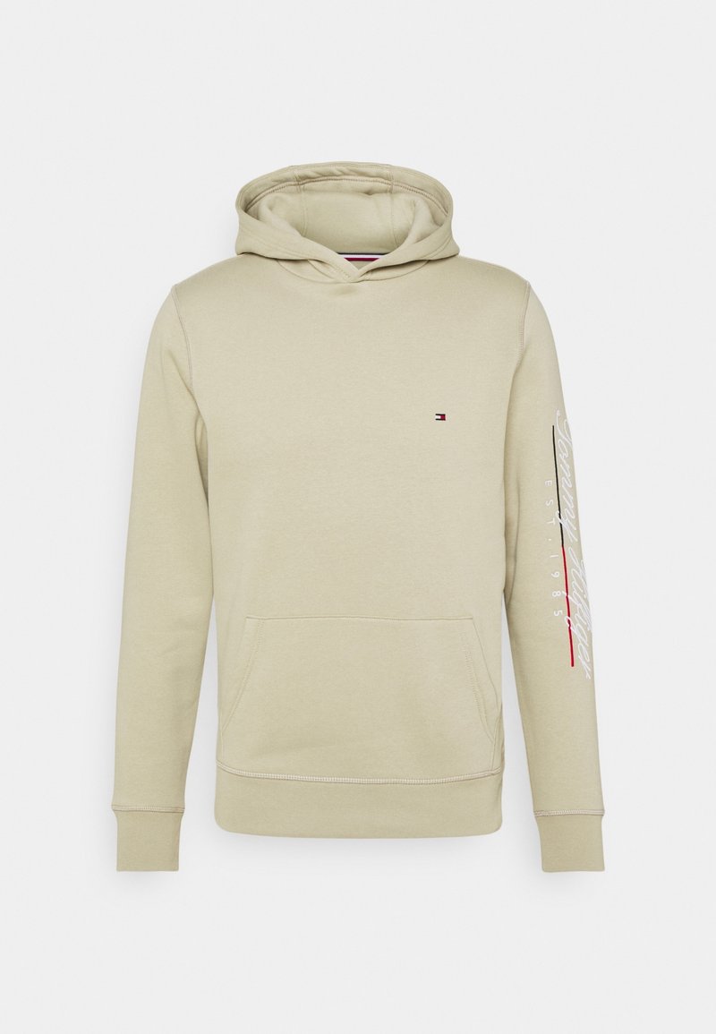 Sweat à capuche beige avec poche frontale, petit logo Tommy Hilfiger sur la poitrine et inscription blanche sur la manche droite.