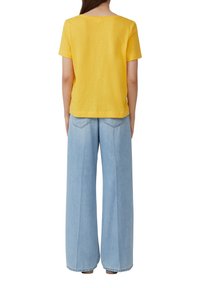 Chemise jaune à manches courtes avec un col rond, associée à un pantalon en denim bleu clair à jambes larges, doté de deux poches arrière et d'une coupe décontractée.