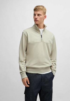 Lichtbeige rits-sweater met een gestructureerd bovenstuk en geribbelde manchetten. Gecombineerd met donkerblauwe cargobroek, die een casual ontwerp laat zien.