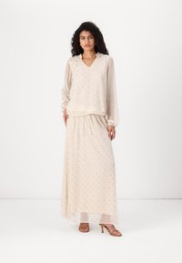Completo beige a due pezzi composto da una blusa a maniche lunghe con scollo a V e un delicato motivo a pois, abbinata a una gonna fluida.