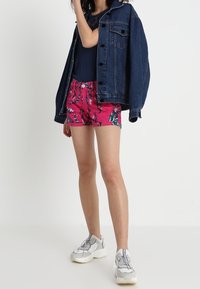 Denim jacket over a navy top, paired with pink floral shorts and gray sneakers. The shorts feature a bold pattern with leaves and flowers.
