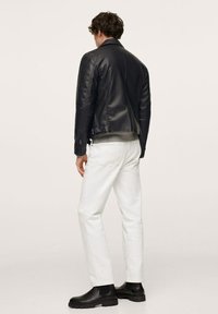 Giacca di pelle nera dal design aderente, polsini con cerniera, dettagli sul retro. Indossata con jeans bianchi e stivaletti Chelsea neri.