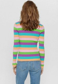 Maglione a maniche lunghe a coste con strisce orizzontali colorate in rosa, arancione, verde, blu e viola. Indossato con jeans azzurri chiari.