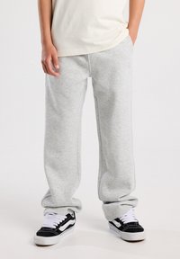 Light gray, cozy sweatpants with a relaxed fit, featuring elastic cuffs and side pockets. Paired with black and white sneakers.