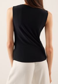Top negro sin mangas hecho de una tela suave, con un diseño de espalda drapeada, complementado con pantalones blancos de corte holgado.