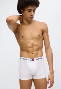 Άσπρα ανδρικά εσώρουχα boxer με απαλό υλικό και ζώνη μέσης με λογότυπο που έχει κόκκινες, άσπρες και μπλε λεπτομέρειες· εφαρμοστό σχέδιο που αναδεικνύει το σχήμα του σώματος.