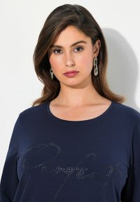 Dunkelblaues Langarmshirt mit rundem Halsausschnitt und silbernem Nieten-Design mit dem Schriftzug "Perfect" auf der Vorderseite. Glatte Stofftextur.