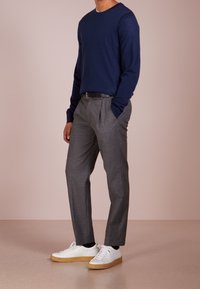 Granatowy sweter z długim rękawem i okrągłym dekoltem w zestawieniu z szarymi spodniami w kant i białymi trampkami o fakturowanej gumowej podeszwie. Prosty design, nowoczesny krój.