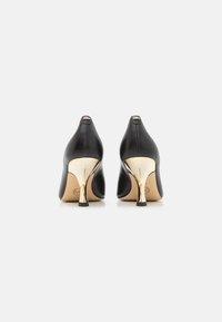 Scarpe nere in pelle con tacco alto e punta affilata, dotate di un accento in metallo dorato sul tacco e una finitura liscia e-texturizzata.