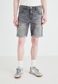 Sive jeans kratke hlače z zavihanimi robovi, zasnova s petimi žepi in rahlim bledežem. V kombinaciji s sivimi športnimi čevlji in belimi kratkimi nogavicami.