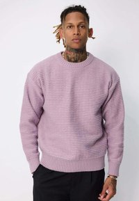 Sweatshirt texturé violet clair à col rond, avec des poignets et un ourlet côtelés. Porté avec un pantalon noir à coupe décontractée.