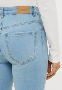 Lys blå denimjeans med en teksturert finish, med et brunt skinnmerke merket "perfekte jeans" og doble baklommer med sydd kanter.
