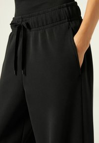 Zwarte joggers van zacht materiaal met een elastische tailleband, trekkoordsluiting en zijzakken. Gladde textuur en een relaxte pasvorm.
