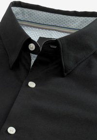 Cămașă neagră cu nasturi, cu un guler elegant. Interiorul are un căptușel cu un model albastru deschis și nasturi albi pentru contrast.