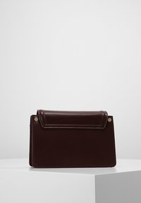 Vinrød læderhåndtaske med en struktureret form, fold-over klap og metalknapp accents. Glat tekstur med synlige syningsdetaljer.