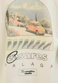 Weißes T-Shirt mit einer Vintage-Illustration eines orangefarbenen Autos auf einer Küstenstraße, mit dem Text "Casares Malaga" und geometrischen Musterelementen.