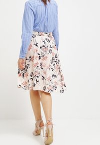 Kukkakirjallinen midi-hame, jossa on vaalea vaaleanpunainen pohja, tummat kukkakuviot, laskokset ja tiukka vyötärö, yhdistettynä vaaleansiniseen raidalliseen paitaan.