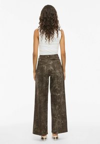 Pantalones de pierna ancha en un estampado de serpiente marrón texturizado, de alta cintura con bolsillos traseros, complementados por una camiseta ajustada blanca.