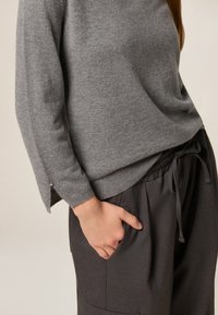 Grauer Strickpullover mit lockerer Passform, hohen Seitenschlitzen und einer glatten Textur, kombiniert mit dunkelgrauen, weit geschnittenen Hosen.