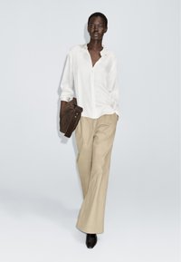 White button-up shirt, beige wide-leg trousers, and a brown bag. The look features clean lines and smooth textures, with pointed black heels.