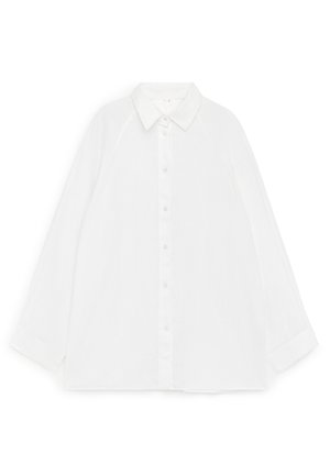 Balta ilgomis rankovėmis susegama marškinėliai su smailiu apykakliu, gulintys ant baltos fono, parodytas priekis.