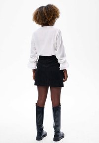 Witte blouse met lange mouwen en geruilde manchetten, zwarte suède minirok en zwarte leren laarzen tot de knie. Gladde textuur, minimalistisch ontwerp.