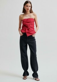 Czerwony top bez ramiączek z asymetrycznym węzłem, zestawiony z luźnymi czarnymi dżinsami z wiązanymi akcentami na nogawkach.