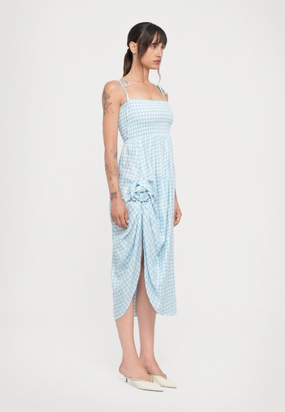 Sininen ja valkoinen ruudullinen mekko, jossa on naruolkaimet, tiukka runko, rypistetty sivuosio ja reisi korkealle ulottuva halkio. Yhdistetty beigeihin korkokenkiin.