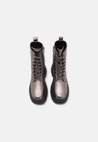 Botas de combate metálicas en gris con cordones frontales, cremalleras laterales y suelas de goma negra gruesa. Presentan una textura suave y altura hasta el tobillo.