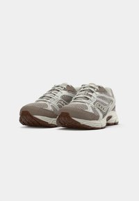 Lightweight athletic shoes with a mesh upper in beige and grey, rubber outsole, padded collar, and reflective accents. Features lacing system.