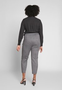 Maglietta nera a maniche lunghe con colletto, infilata in pantaloni a quadri alla caviglia con vita aderente e texture liscia.