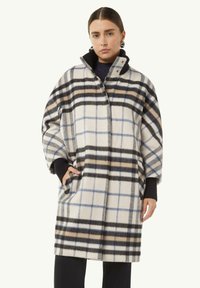 Karierten Wollmantel mit hohem Kragen, oversized Schnitt, Taschen und einer Farbpalette aus weißen, schwarzen, blauen und braunen Linien.