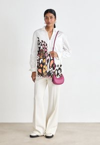 White shirt with colorful abstract pattern on one side, paired with cream wide-leg trousers and a small pink crossbody bag.