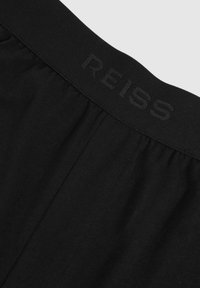 Schwarzer Stoff in Nahaufnahme mit elastischem Bund und subtiler "REISS"-Markierung in passenden schwarzen Buchstaben.
