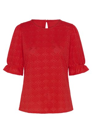 Červená blúzka s krátkym rukávom a geometrickým čipkovaným vzorom, okrúhlym výstrihom s malým otvorom na chrbte a volánikovými lemami rukávov.